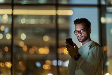 Man looks at smartphone in a dark city apartment.