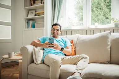 Man uses smartphone while sitting on a couch.