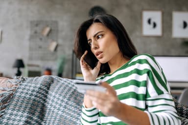Woman holding a credit card talks on the phone.