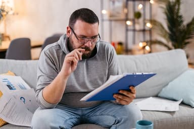 Man looks at paperwork while sitting on a couch.