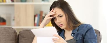 Concerned woman reading letter from bank sitting on a couch in the living room at home