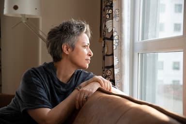 Woman sits on couch and looks out the window.