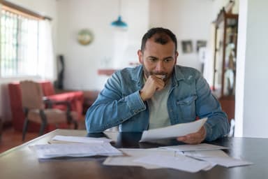 Man looks worried while reading financial paperwork.