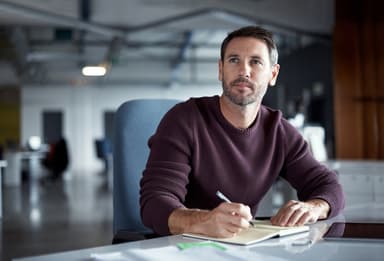 Man writing in a notebook while sitting at a desk.