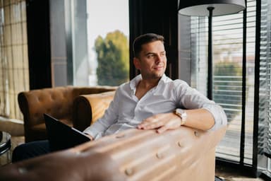 Man sitting on a couch with a laptop looks contemplative.