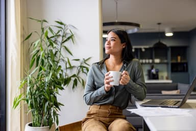 Woman drinks coffee while sitting in front of a laptop.