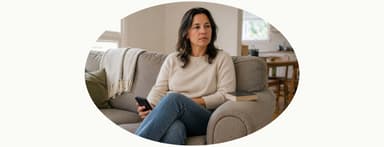 Woman on a sofa holds a phone, looking away thoughtfully.