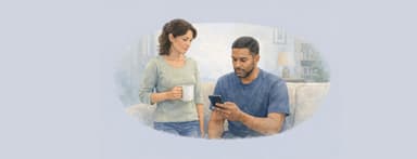 Young couple in living room. Woman standing and drinking coffee. And Man on couch looking at phone.