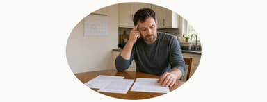 Man rests his head on his hand, looking at documents on a table.