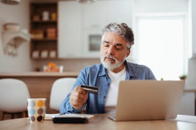 Man contemplates credit card while sitting at a laptop.