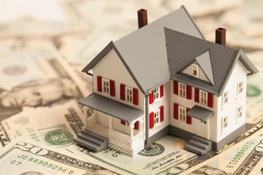 Plastic house model on top of $20 bills.